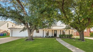 A single-story house with a garage, a well-maintained lawn, and two large trees in front.