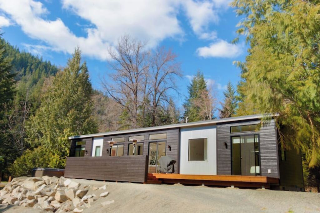 A modern cabin with a wooden deck, large windows, and a view of the surrounding forest.