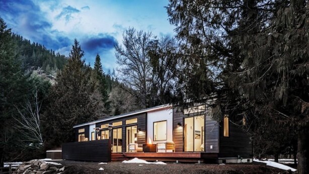 Eine moderne Holzhütte mit großen Fenstern, einer Terrasse und Blick auf den umliegenden Wald.