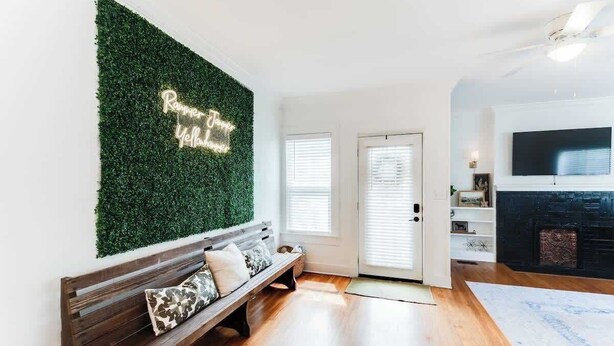 A living room with a wooden bench, a green wall with a neon sign, a fireplace, and a television mounted on the wall.