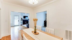 A dining area with a wooden table, white chairs, and a vase of dried plants.