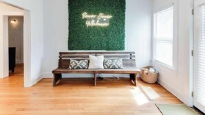 A room with a wooden bench, a green wall with a neon sign, and a window with blinds.
