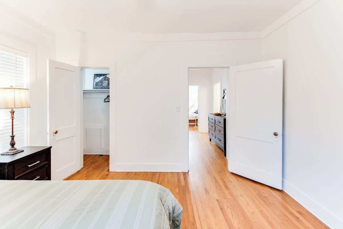 A bedroom with a bed, a dresser, and a lamp. There are white doors and a hallway leading to another room.