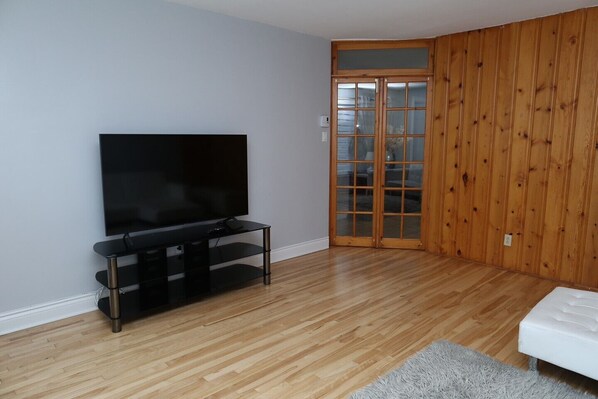 A room with a TV on a black stand, wooden flooring, a white sofa, and a sliding glass door.