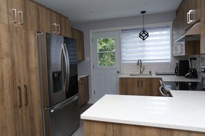 A modern kitchen with wooden cabinets, stainless steel appliances, a white countertop, and a window with blinds.