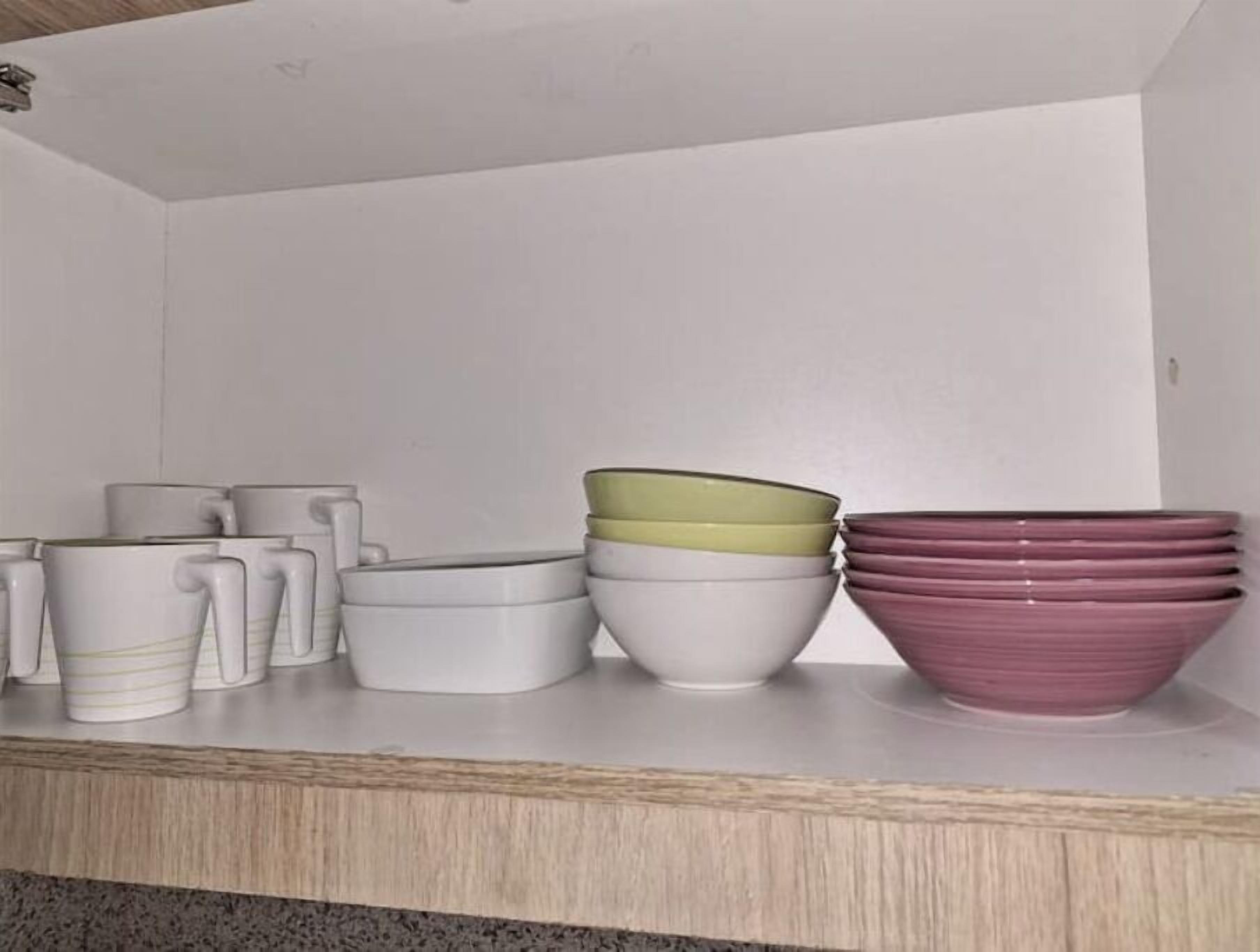 Una cuina amb un taulell ple de bols i tasses de colors diverses.