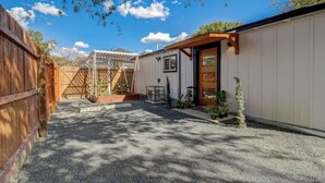 A covered outdoor area with a gravel path, wooden fence, and a small building with a door and windows. - The Southtown Hummingbird Haus (San Antonio)