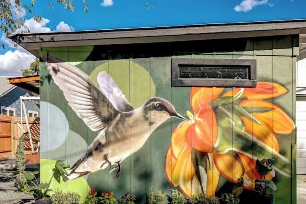 A mural of a hummingbird and flowers on a building's exterior wall.