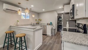 A modern kitchen with a central island, white cabinetry, and a built-in washer and dryer. - The Southtown Hummingbird Haus (San Antonio)