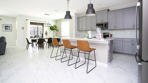 A modern kitchen with grey cabinets, a stainless steel refrigerator, and a bar area with stools.