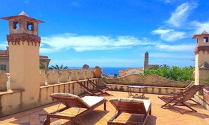 Une terrasse sur le toit, avec des chaises longues, une table et une vue sur la mer et les tours historiques.