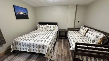 A bedroom with two beds, a wooden floor, a ceiling light, and a framed picture on the wall.