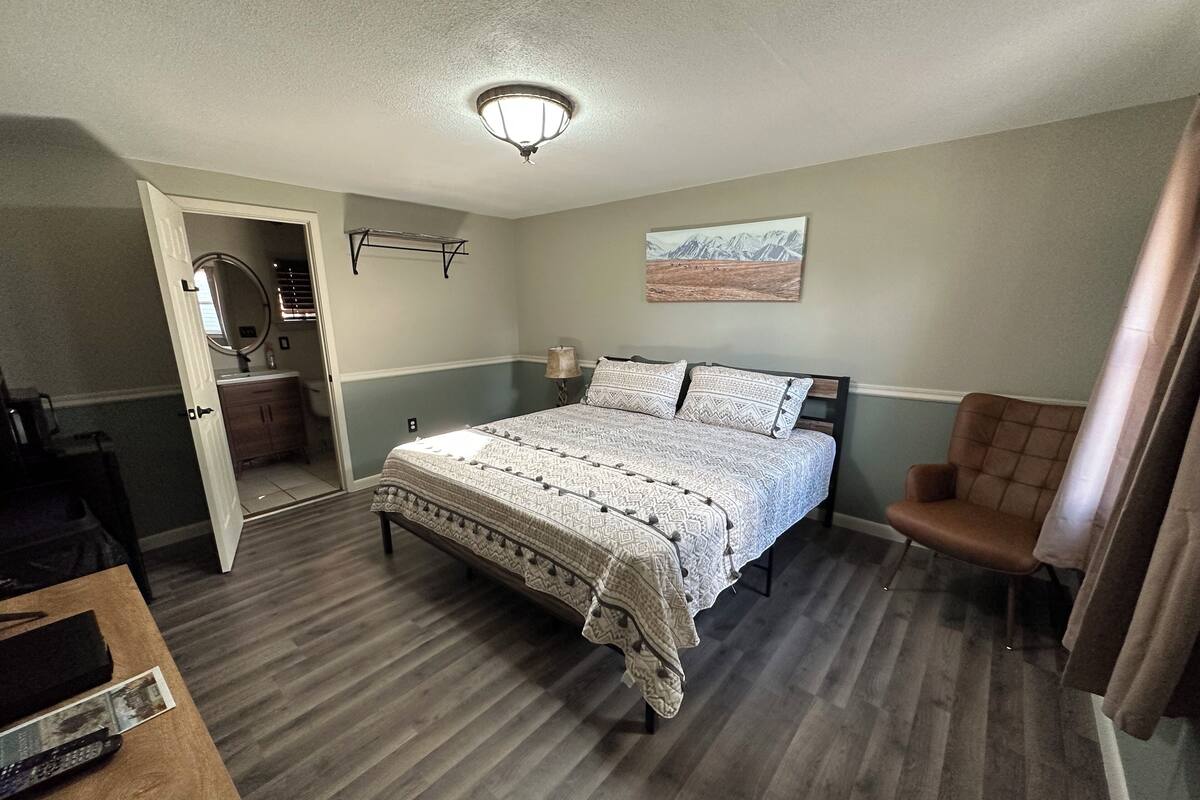 A bedroom with a bed, a chair, a desk, and a painting on the wall.