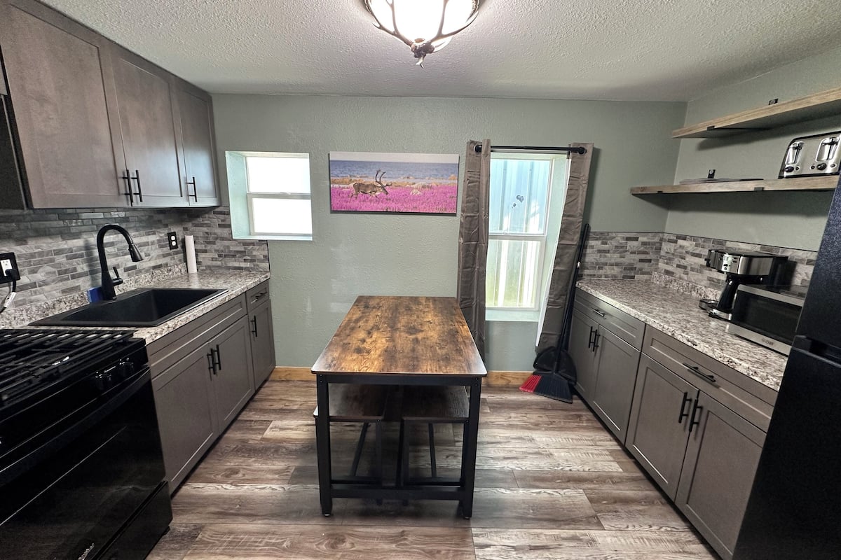 A kitchen with a wooden table, granite countertops, and a backsplash of gray tiles.