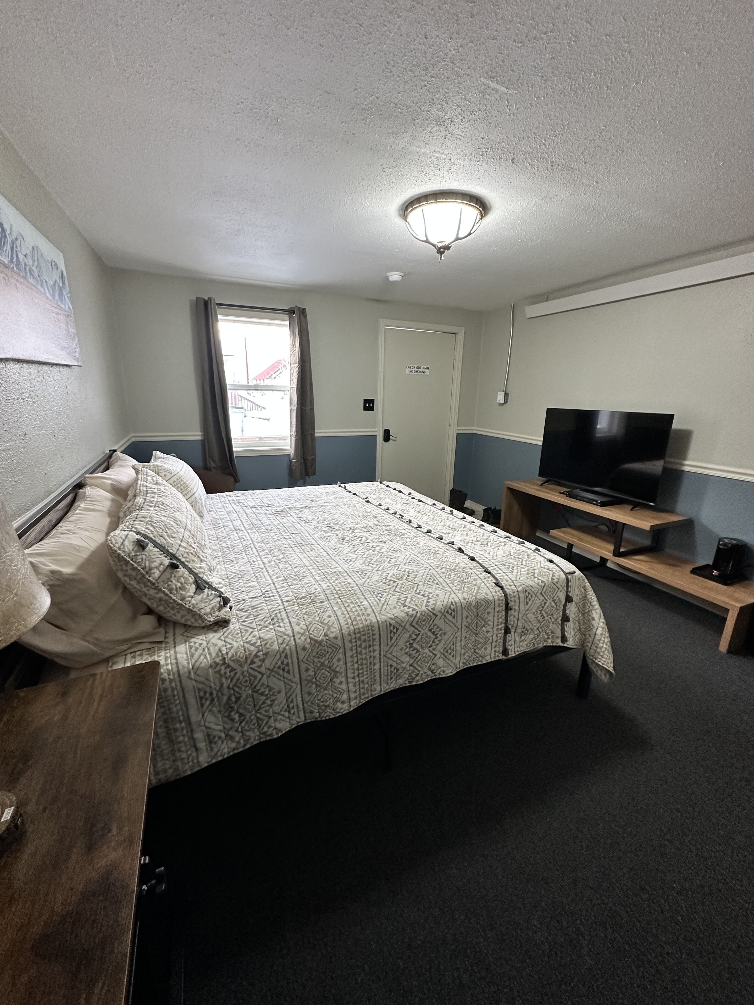 A hotel room with a bed, a television on a wooden stand, a desk with a telephone, and a door with a sign.