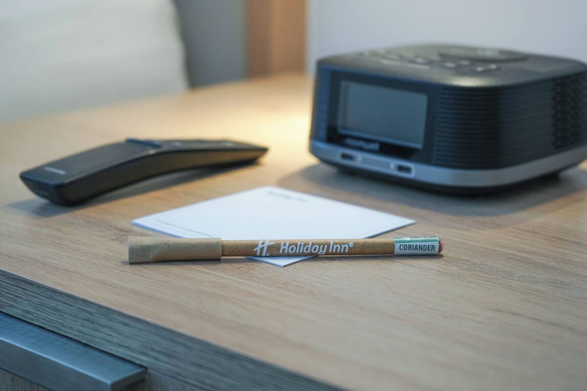A wooden table with a remote control, a small electronic device, and a pencil with "Holiday Inn" branding.