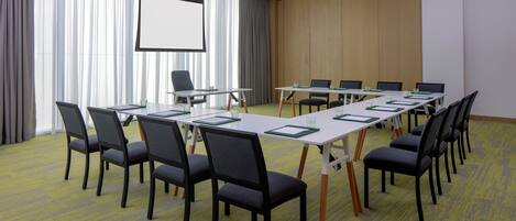 A conference room with a long table, chairs, a projector screen, and a large window with curtains.