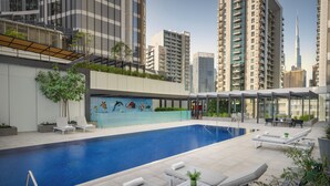 Una piscina en la azotea con sillones de descanso y un mural, rodeada de edificios altos.