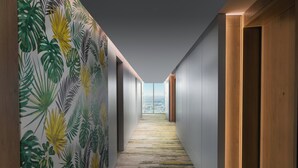 Un pasillo con papel tapiz tropical, puertas de madera y suelo alfombrado que conduce a un ventanal grande.