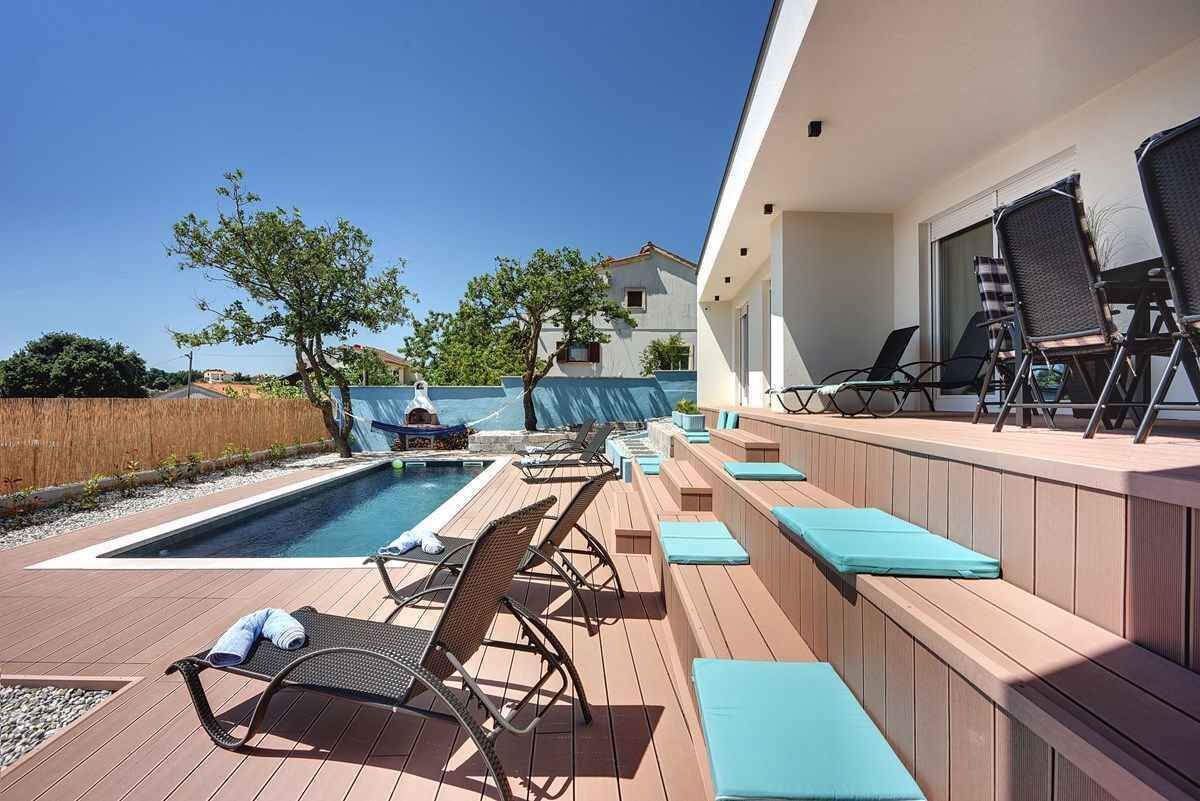 Un área junto a la piscina con sillones de descanso y una terraza de madera.