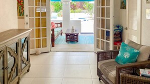 An open doorway leading to a pool area with a wicker sofa and a small table. - Tropical Oasis with Pool close to beach - Beachcomber (Sunset Crest)