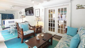 A living room with a sofa, two chairs, a coffee table, a TV, and a door leading to another room. - Tropical Oasis with Pool close to beach - Beachcomber (Sunset Crest)