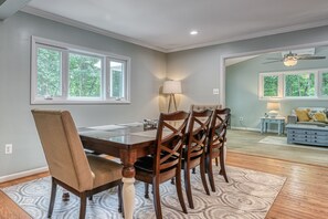 Un comedor con una mesa y sillas de madera, una lámpara y vistas al exterior a través de grandes ventanales.