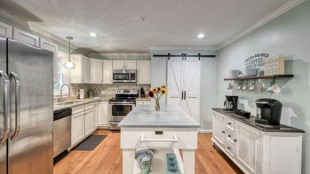 A modern kitchen with white cabinets, stainless steel appliances, a central island, and a hanging pot rack.