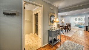 A hallway with a laundry room, a console table with a mirror, and a dining area with chairs and a table.