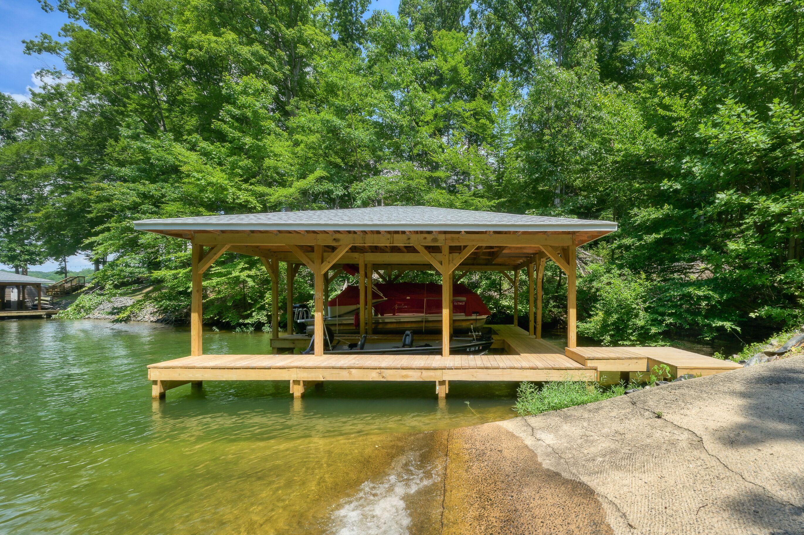 A wooden dock extending into a lake, with a covered seating area and a boat docked nearby.