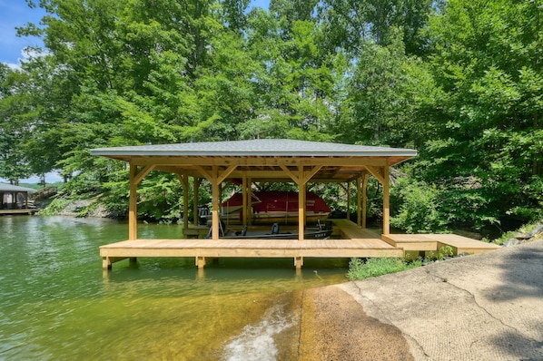 A wooden dock extending into a lake, with a covered seating area and a boat docked nearby.