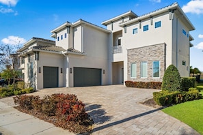 A two-story residential building with a driveway, garage, and landscaped garden. - Chateau at Bear's Den: Pool, Arcade Games, Golf Views, Free Water Park (Kissimmee)