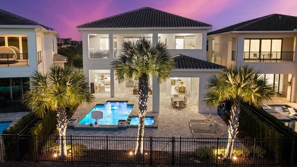 A two-story house with a swimming pool, surrounded by palm trees and a fence. - Chateau at Bear's Den: Pool, Arcade Games, Golf Views, Free Water Park (Kissimmee)