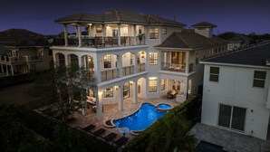 Ein mehrgeschossiges Haus mit großem Schwimmbecken, Sitzgelegenheiten im Freien und einer überdachten Terrasse.