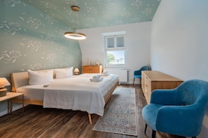 Une chambre à coucher comprenant un lit, une table de chevet, une lampe, une chaise, un bureau et une fenêtre donnant sur un paysage agréable.
