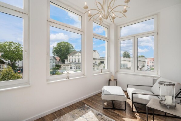 A room with large windows, a chandelier, and a view of a residential area.