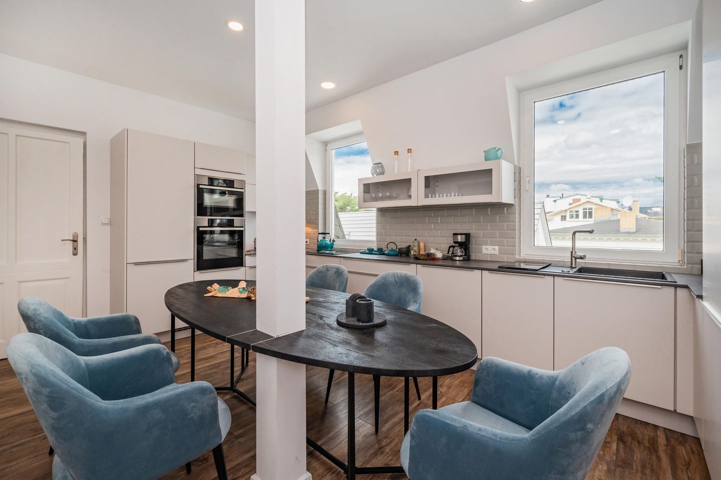 Una cocina moderna con armarios blancos, encimera negra y ventana con vistas a una zona residencial.