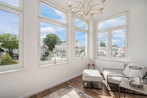 A room with large windows, a chandelier, and a view of a residential area.