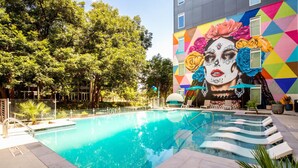 A swimming pool with a mural of flowers and geometric patterns on the adjacent building. - Riverwalk Luxe Apartment, Stunning pool, King Bed (San Antonio)