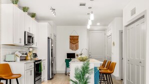 A modern kitchen with white cabinetry, a central island with stools, a microwave, oven, and a sink. - Riverwalk Luxe Apartment, Stunning pool, King Bed (San Antonio)