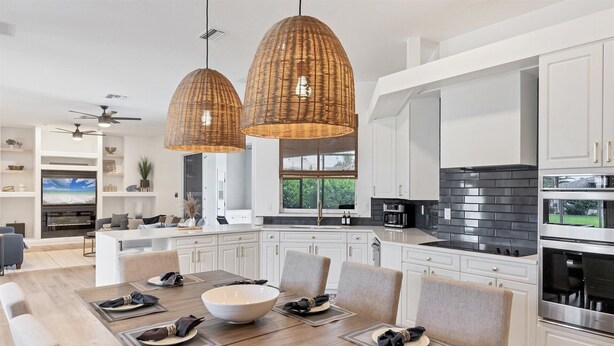 A modern kitchen with white cabinetry, a black tiled backsplash, and a dining area with a large table set for six. - Waterfront Punta Gorda Isles Retreat: Private Pool & Charlotte Harbor Canal Access (Punta Gorda)