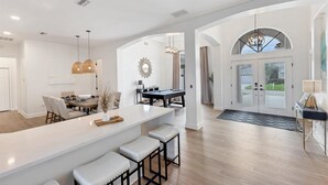 A spacious kitchen with a central island, a dining area with a pool table, and a large arched doorway leading to an outdoor area. - Waterfront Punta Gorda Isles Retreat: Private Pool & Charlotte Harbor Canal Access (Punta Gorda)
