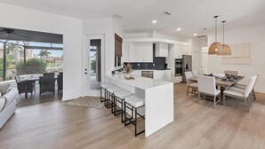 A modern kitchen with white cabinetry, a central island, and a dining area with a table and chairs. - Waterfront Punta Gorda Isles Retreat: Private Pool & Charlotte Harbor Canal Access (Punta Gorda)