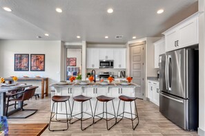 Una cocina moderna con armarios blancos, un refrigerador de acero inoxidable y una isla central con taburetes de bar.