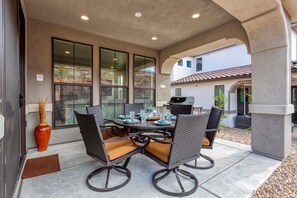 Eine Terrasse im Freien mit einem runden Tisch, vier Stühlen und einem Grill.
