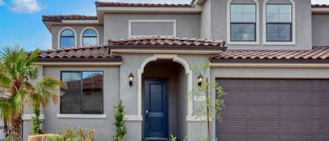 A two-story house with a dark blue front door, a garage door, and a landscaped front yard with rocks and plants.