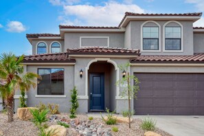 A two-story house with a dark blue front door, a garage door, and a landscaped front yard with rocks and plants.