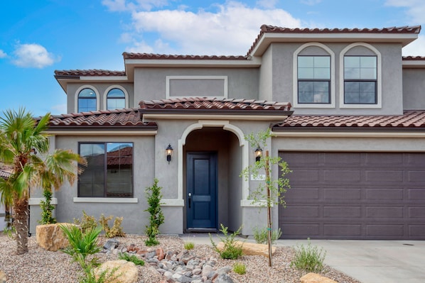 A two-story house with a dark blue front door, a garage door, and a landscaped front yard with rocks and plants.