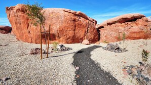 Paisaje desértico con grandes formaciones rocosas rojas y un camino de grava que las lleva al fondo.