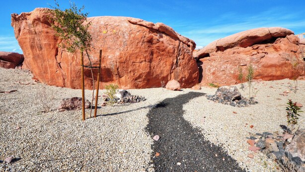Paisaje desértico con grandes formaciones rocosas rojas y un camino de grava que las lleva al fondo.